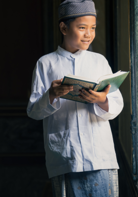 A young Quran student respectfully picking up the Holy Quran with both hands.
