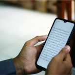 A smartphone displaying an open Quran app with clear Arabic text, placed on a prayer mat or held in someone’s hand.