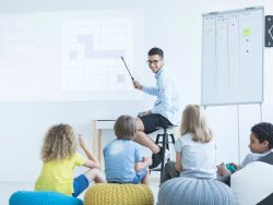 Group of schoolchildren in a bright, modern classroom with colorful furniture, digital screens, and engaging learning materials.